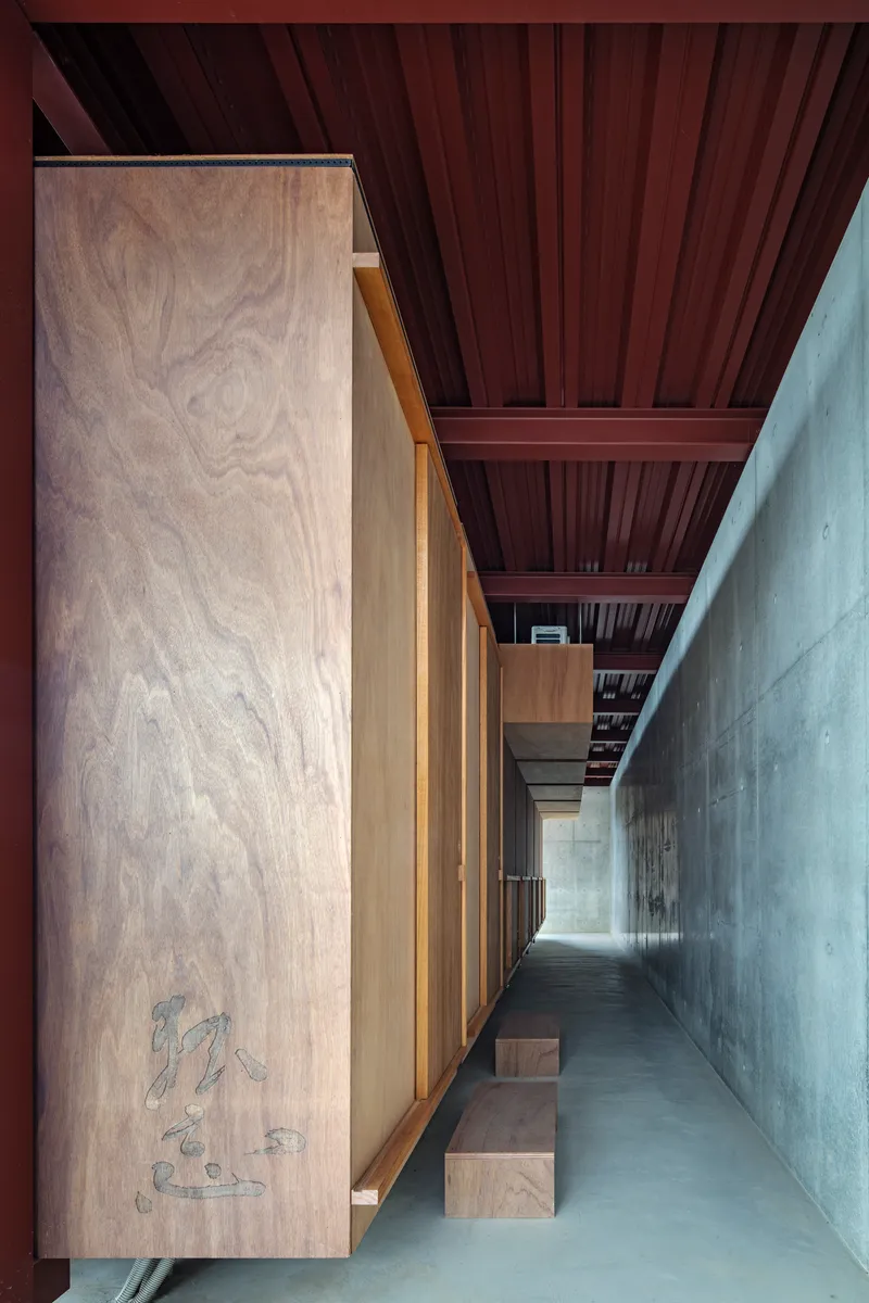 Interior corridor with plywood cabinetry and corrugated metal ceiling between concrete walls