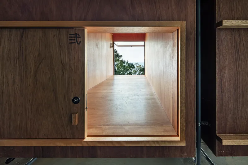 Sliding wood panel revealing a plywood-lined passage to a window overlooking the sea