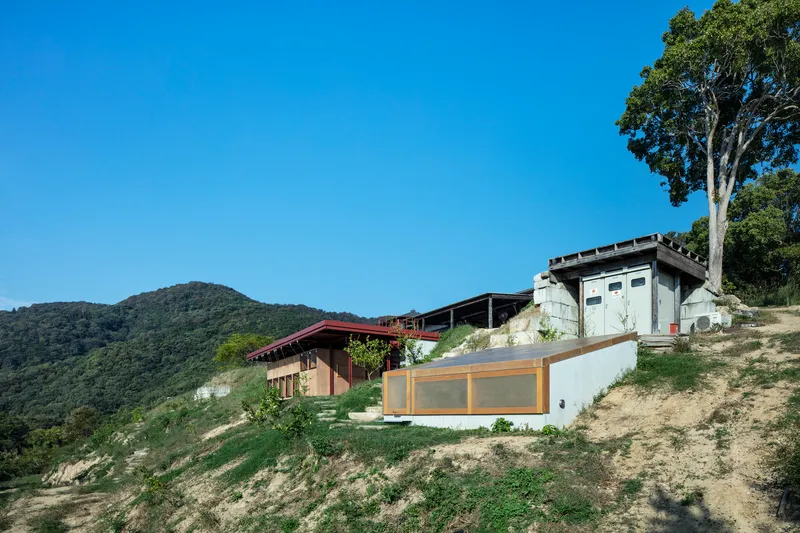 Compound of stepped volumes on grassy slope with forested hills in the background