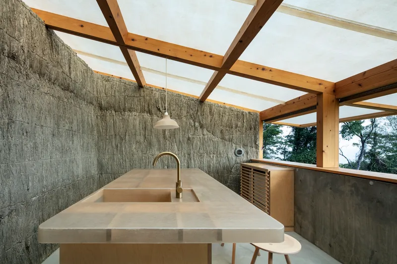 Kitchen counter with stone surface under exposed timber rafters and translucent skylight panels