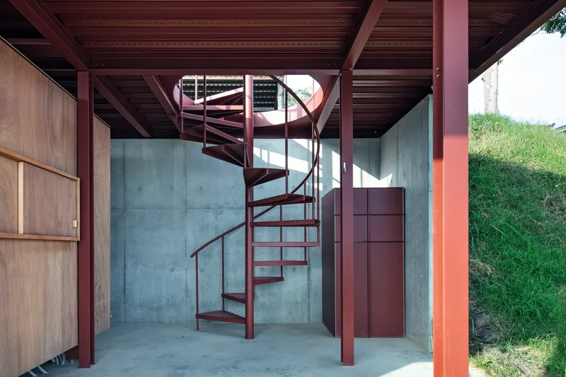 Red spiral stair rising through space with exposed steel columns and concrete walls