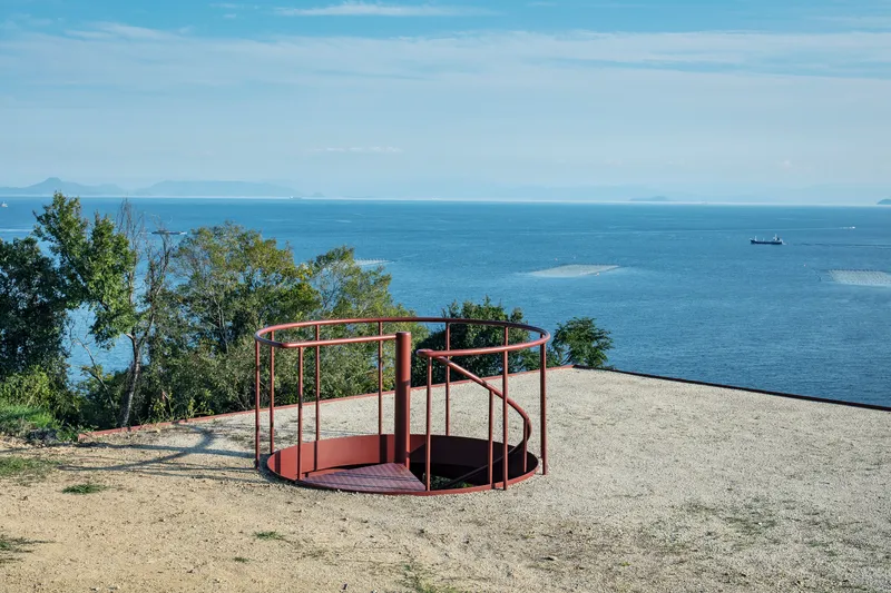 Circular steel-framed observation platform on the gravel terrace with ocean views beyond