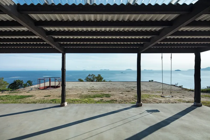 Covered terrace with corrugated roof and steel columns overlooking coastal landscape with swing