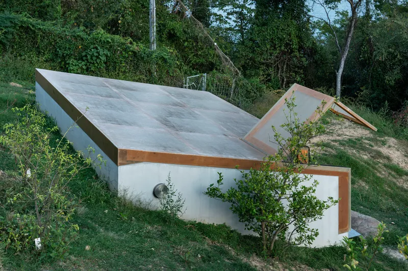 Angular concrete roof planes with timber edges emerging from a sloped grassy site