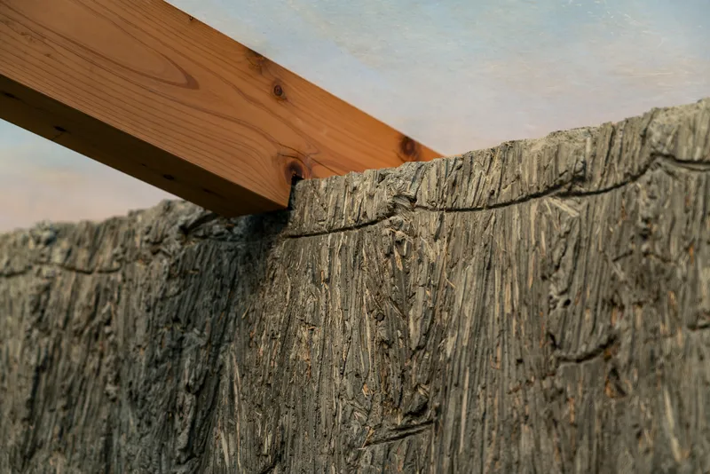 Detail of timber beam meeting the textured hempcrete wall under a white ceiling panel