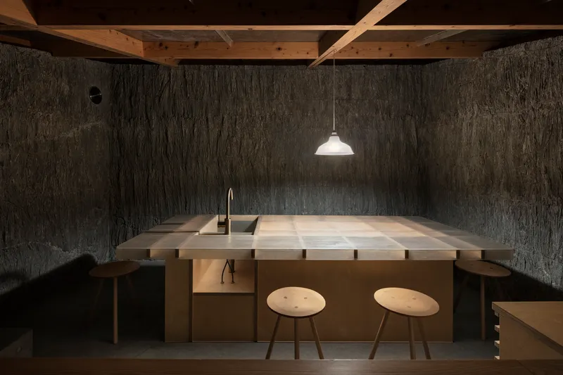 Kitchen counter with sink and two stools beneath exposed timber beams and pendant light