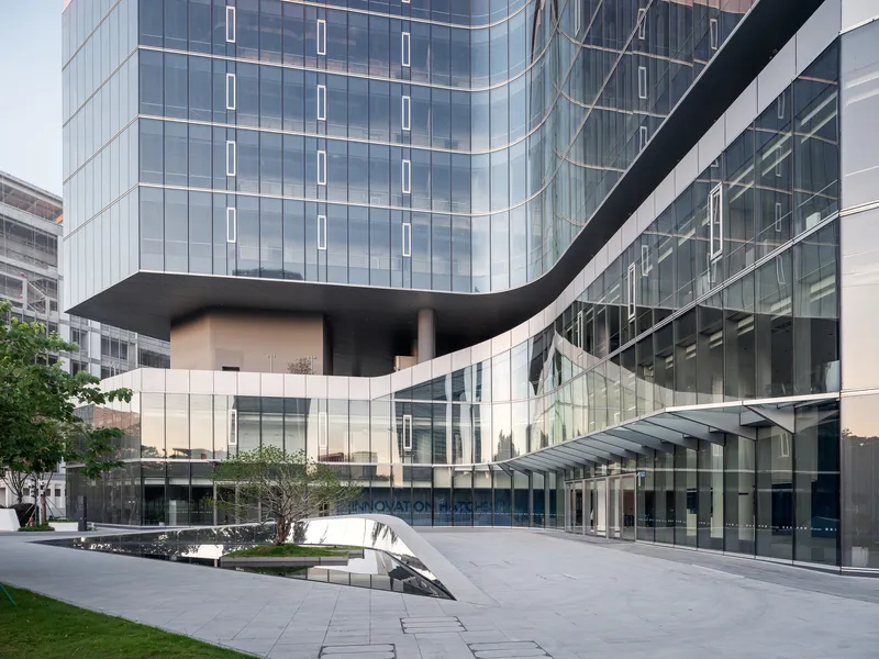 Ground-level courtyard with curved entry canopy and reflective water feature beneath glass curtain wall