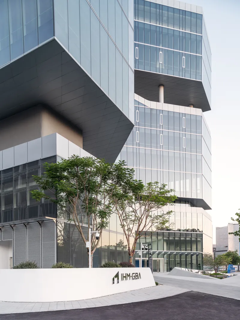 Street view of the stacked glass volumes with cantilevered dark slabs and a mature tree at the entrance