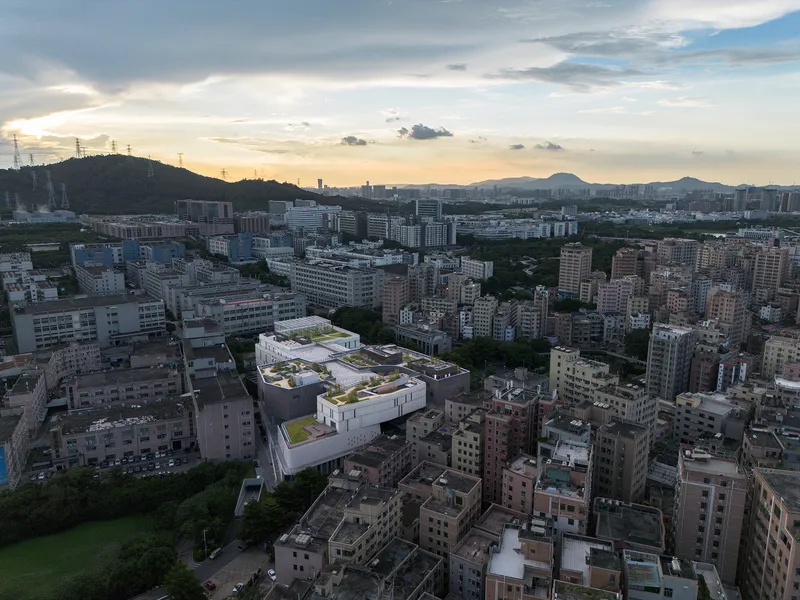 Aerial view of a white rooftop with planted green terraces nestled among dense residential towers at dusk