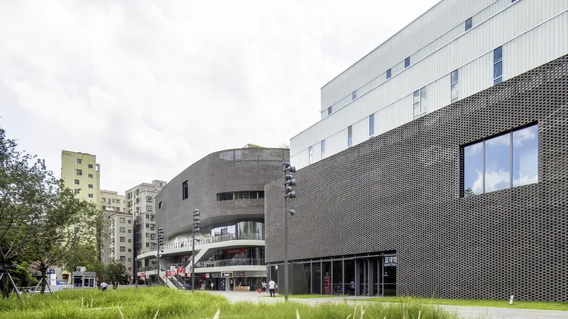 Perforated metal facade wrapping curved volumes beside a grassy lawn with trees on an overcast day