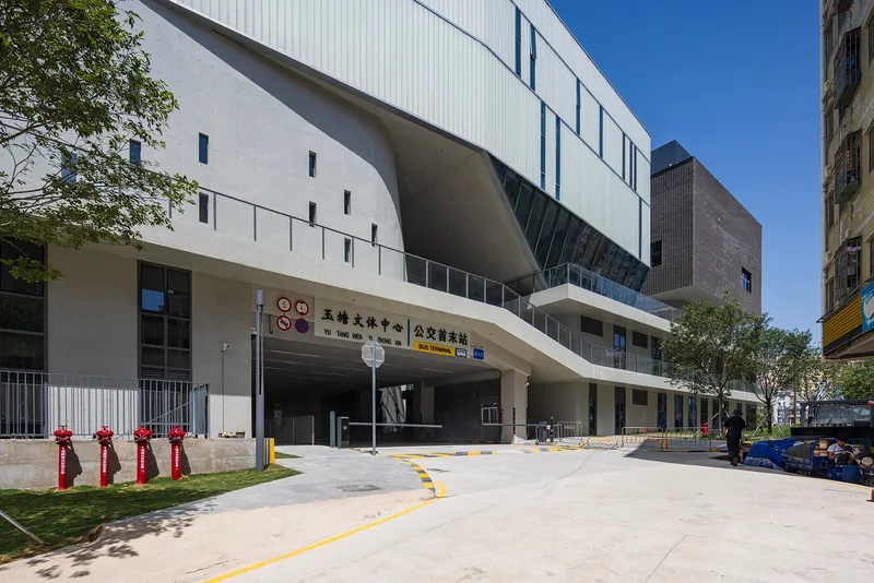 Covered entrance driveway with exposed concrete ceiling flanked by white metal cladding under clear blue sky