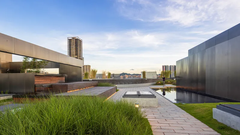 Rooftop terrace with reflecting pool, paved walkways, planted grasses and dark metal perimeter walls at dusk