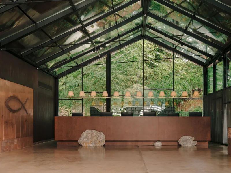 Reception desk in weathered steel beneath a gabled glass roof and suspended pendant lights