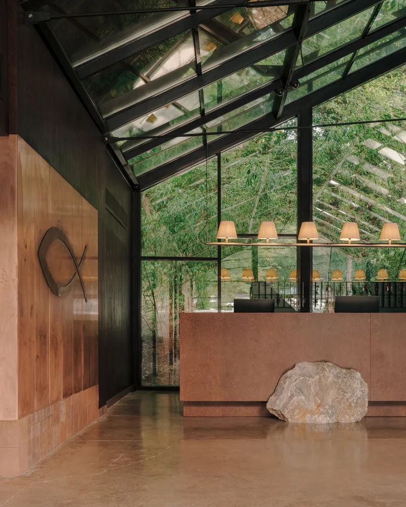 Reception area beneath a glass gable roof with bamboo growing outside steel-framed windows