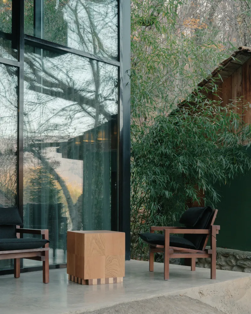 Seating area with timber furniture beside floor-to-ceiling glazing and bamboo in afternoon light