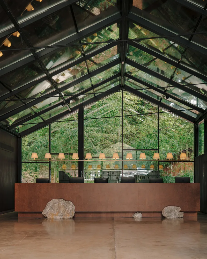 Pitched glass roof with black steel framework above a timber reception desk and pendant light row