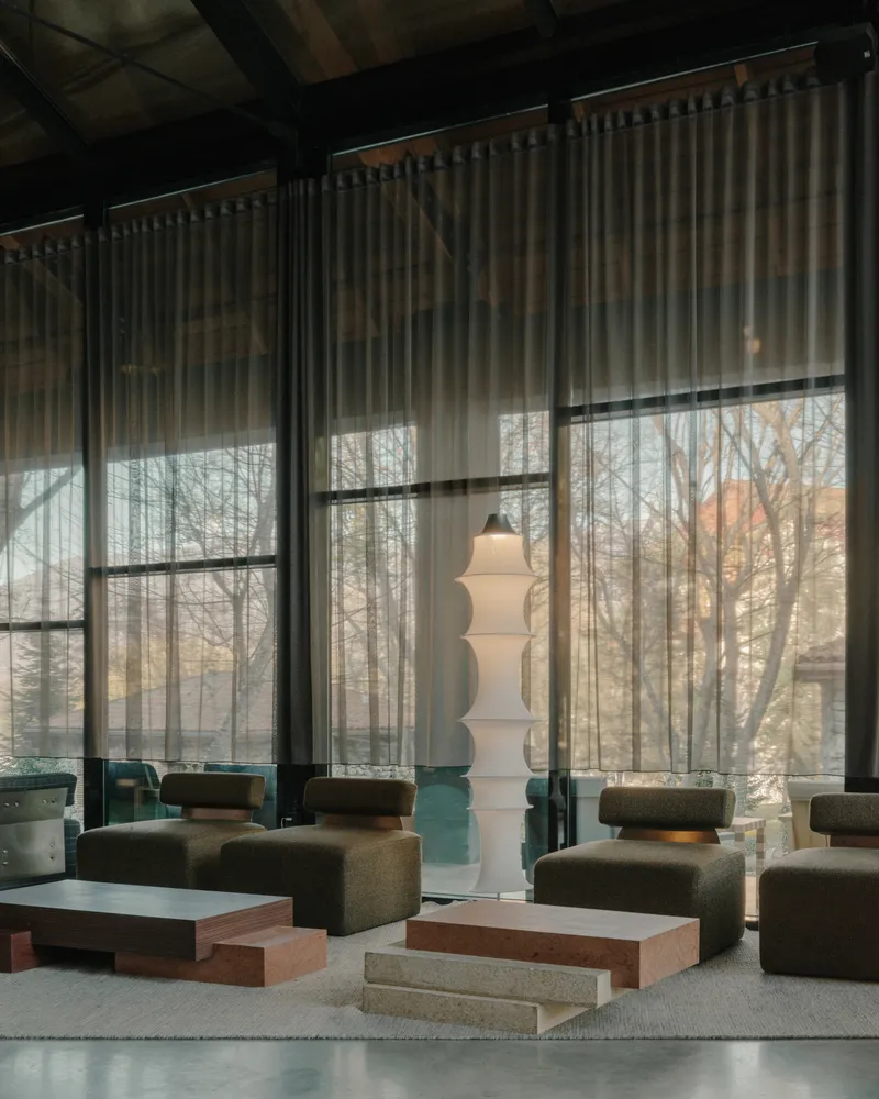 Lounge area with sheer curtains filtering daylight through steel-framed windows overlooking bare winter trees