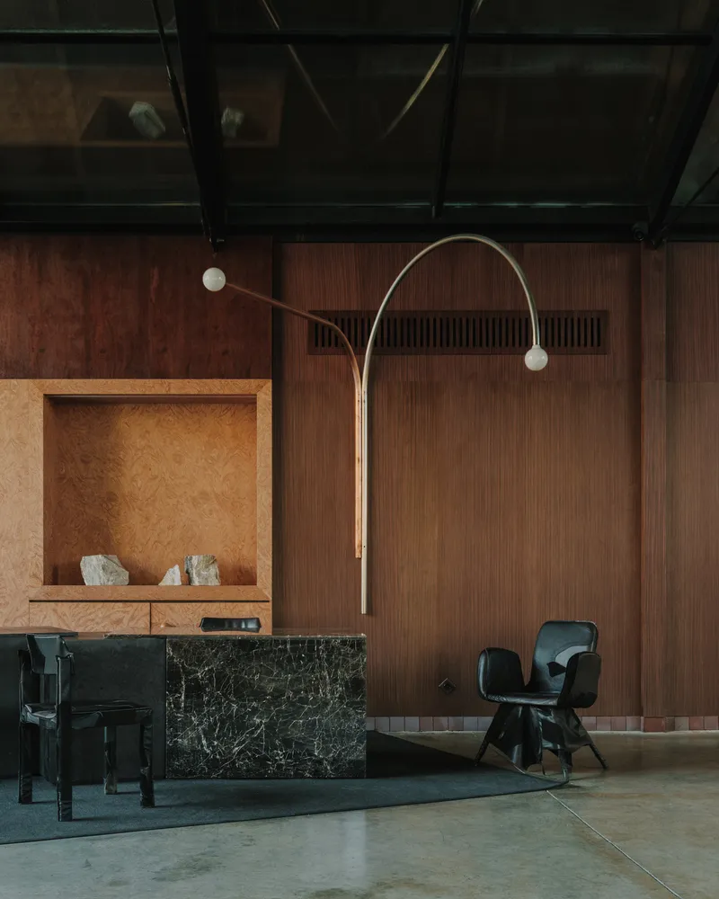 Arcing brass floor lamp beside a timber niche with raw stone fragments against walnut paneling