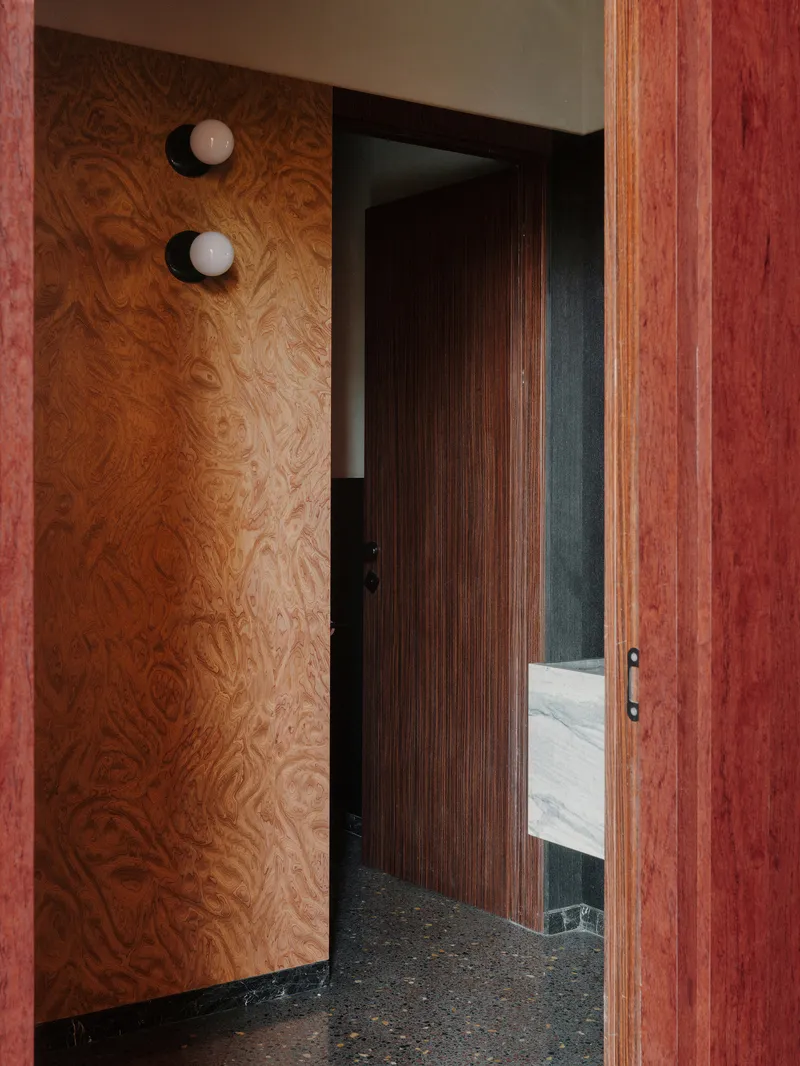 Plywood wall with two circular sconces beside a vertically grooved timber door
