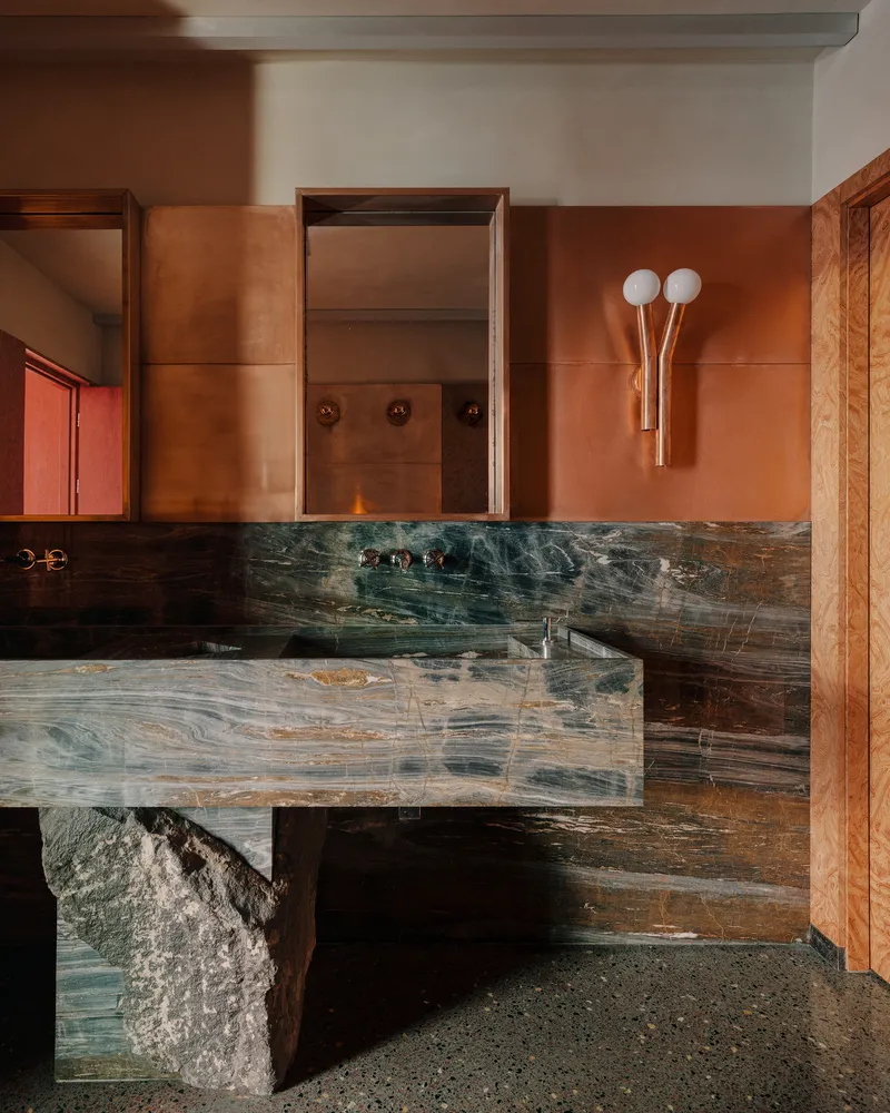 Floating vanity in dark veined stone with copper tile backsplash and terrazzo floor