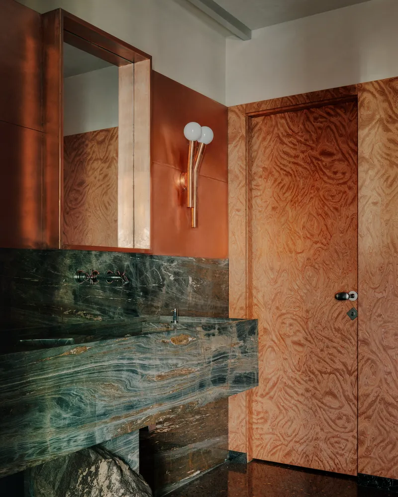 Bathroom corner with copper-clad cabinetry, plywood door, and floating stone vanity below mirror