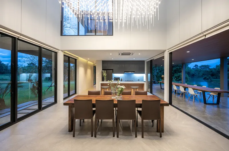 Open-plan dining and kitchen space with sliding glass walls opening to the lawn at twilight