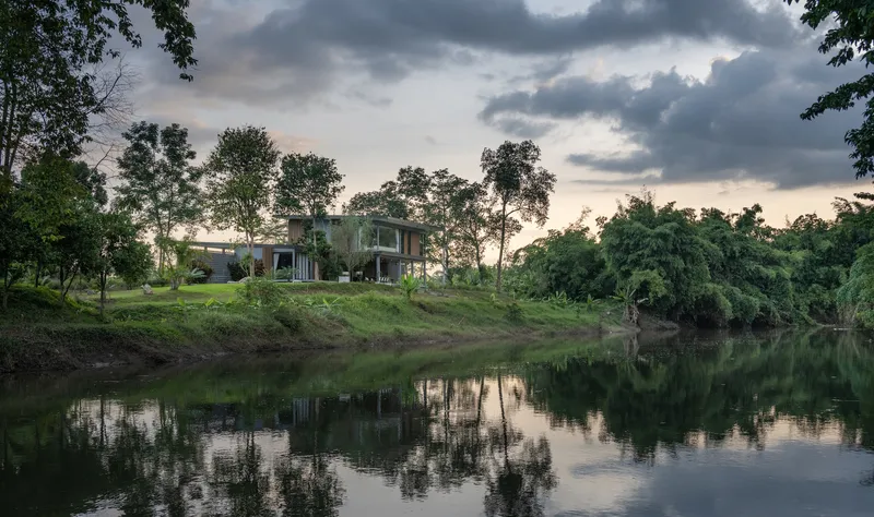 Riverbank view of the residence under dramatic clouds with water reflection