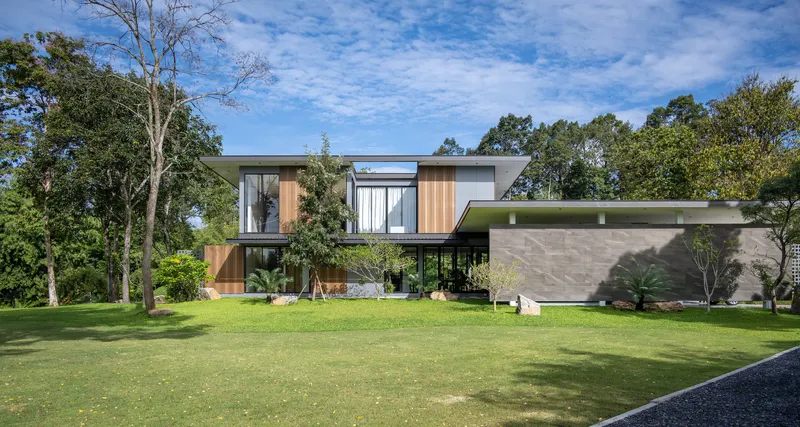 Two-story volume with mixed cladding of timber screens and grey stone across a broad lawn