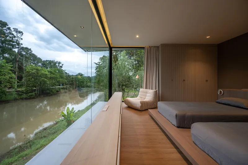 Timber floored bedroom with floor-to-ceiling glass opening onto a river view at dusk