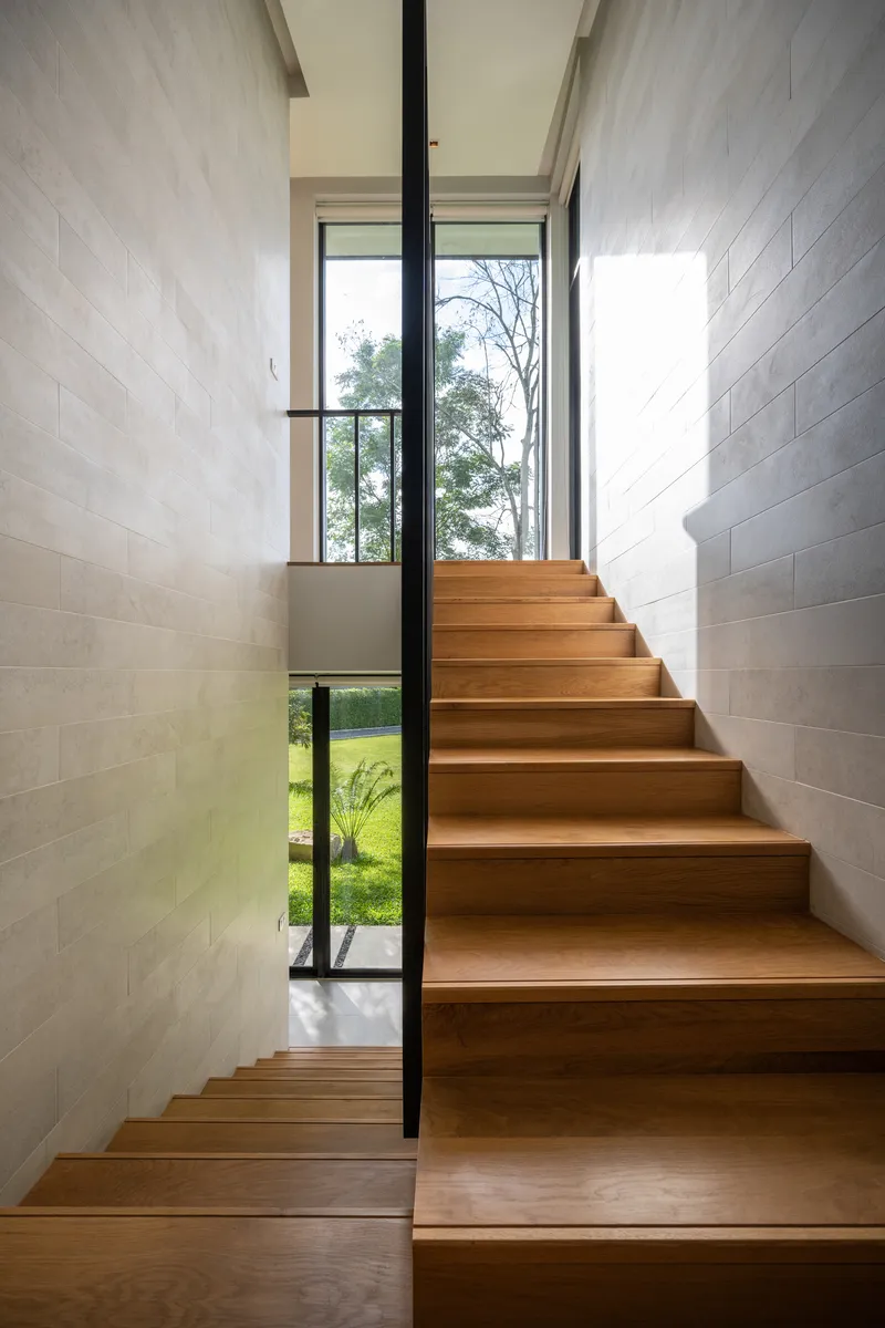 Timber staircase flanked by pale stone walls with black steel handrail and garden view