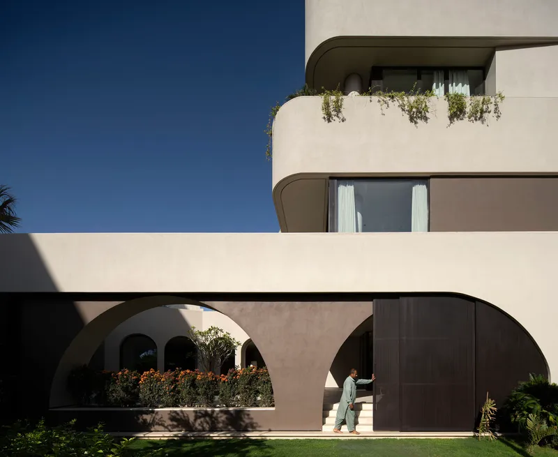 Facade detail showing stacked rounded balconies with trailing plants and resident walking beneath arched passageway