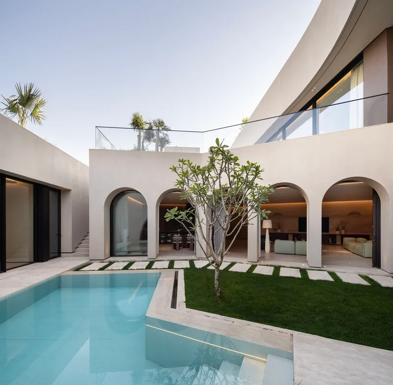 Interior courtyard with rectangular pool and lawn grid pavers beside arched openings at dusk