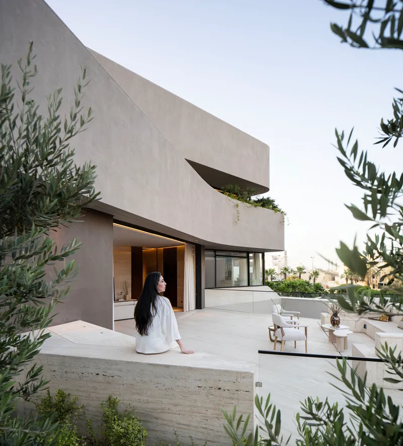 Roof terrace with cantilevered planter and woman in white seated near olive trees at twilight