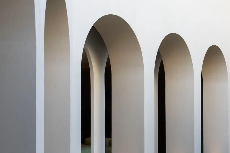 Sequence of tall arched openings with smooth plaster reveals receding into shadow