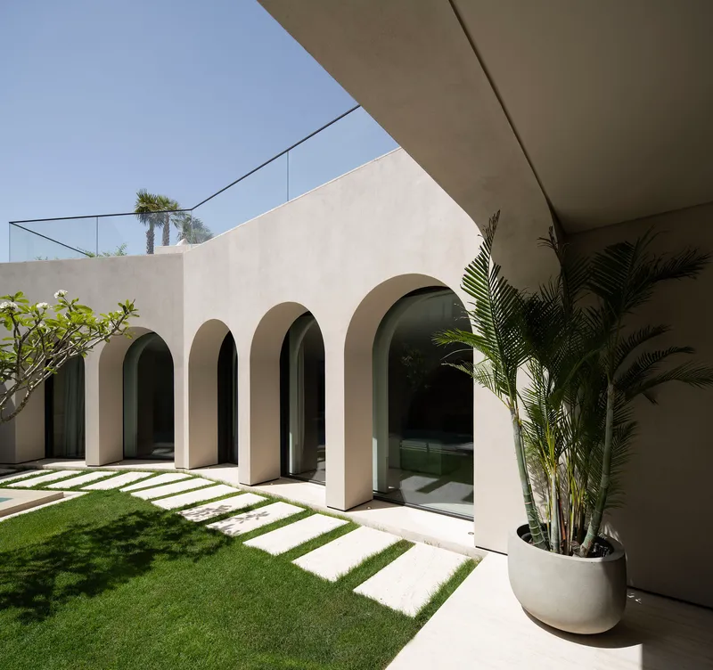 Courtyard arcade with arched doorways flanking a lawn with stone pavers and potted palm