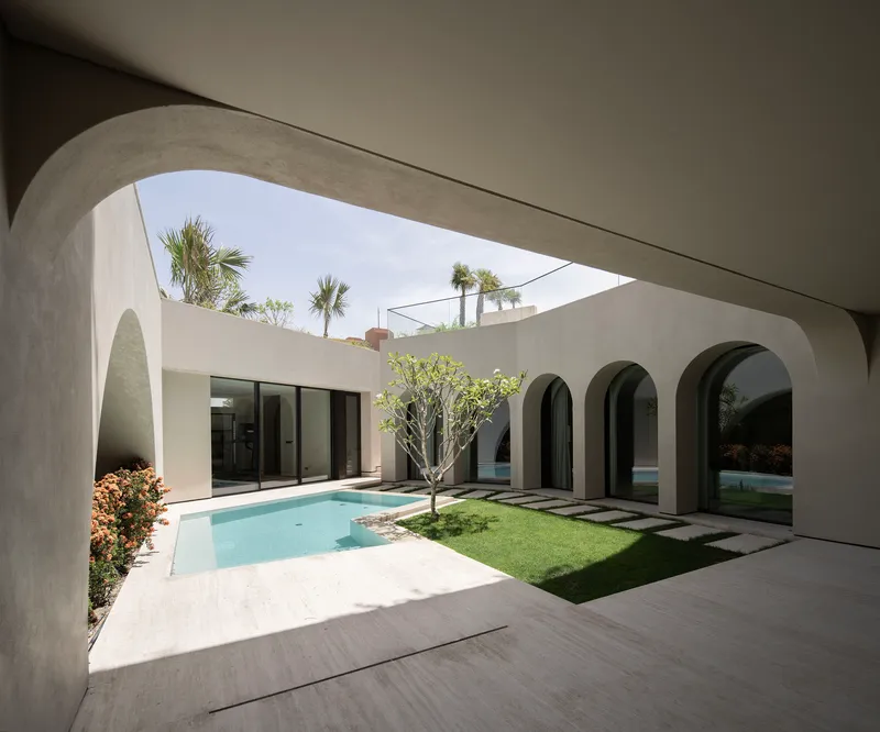 Courtyard view through rounded arches showing a rectangular pool and grass patch bordered by palm trees