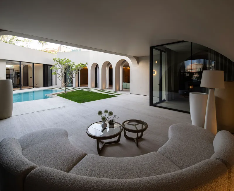 Indoor-outdoor living space opening through arched openings to the pool courtyard beyond at dusk