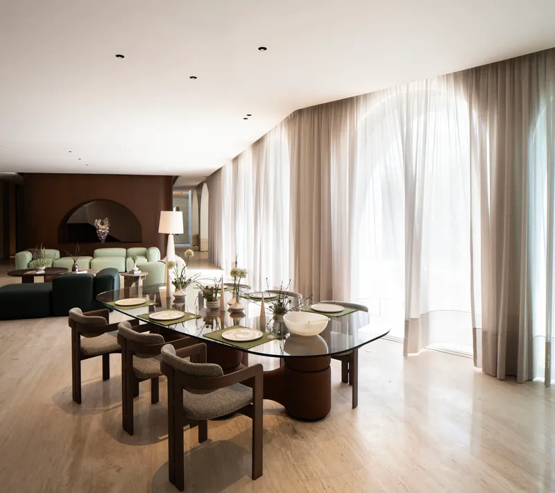 Dining area with floor-to-ceiling sheer curtains filtering daylight across pale timber flooring