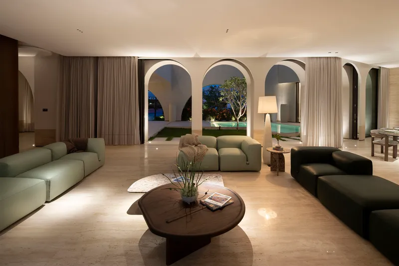 Open-plan living room at twilight with arched openings framing the illuminated garden and tree