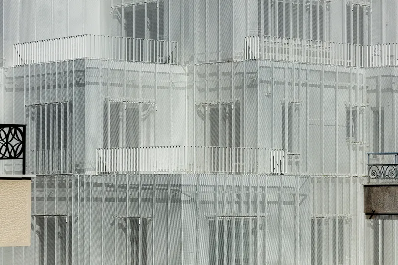 Close-up of the translucent perforated metal panels and vertical louvers wrapping the upper floors