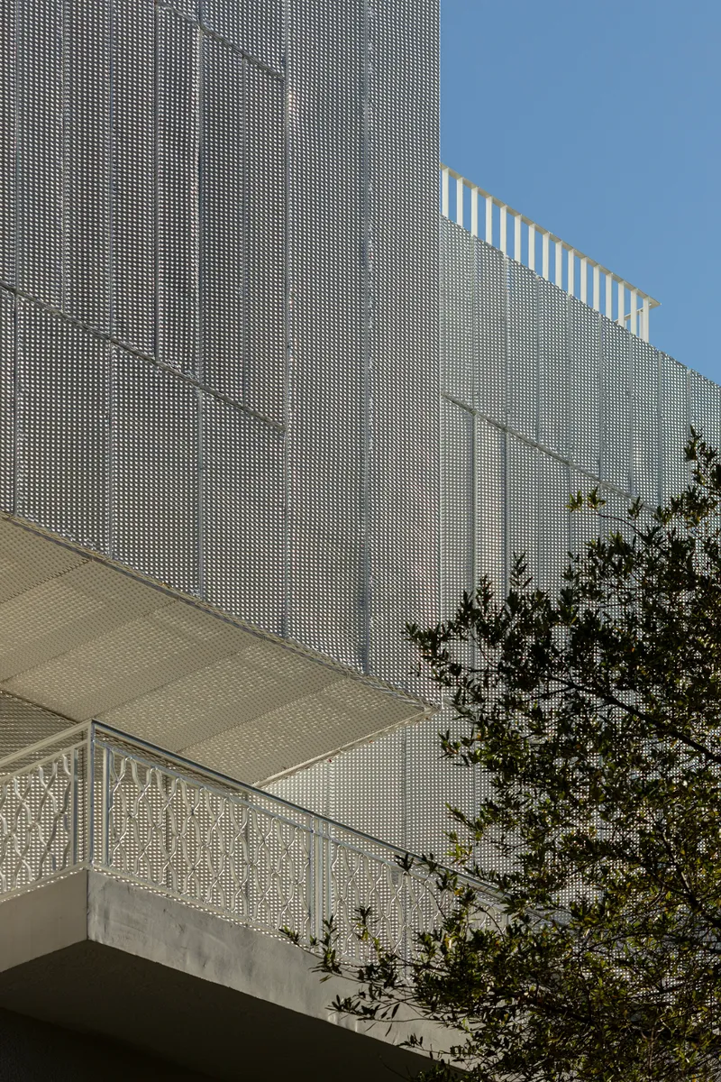 Angled view of the perforated metal screen wall with rooftop pergola slats against a clear sky
