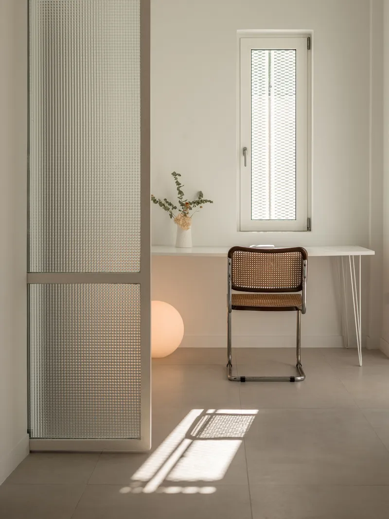 Interior room with perforated sliding panels, work desk, and cane chair bathed in afternoon sunlight
