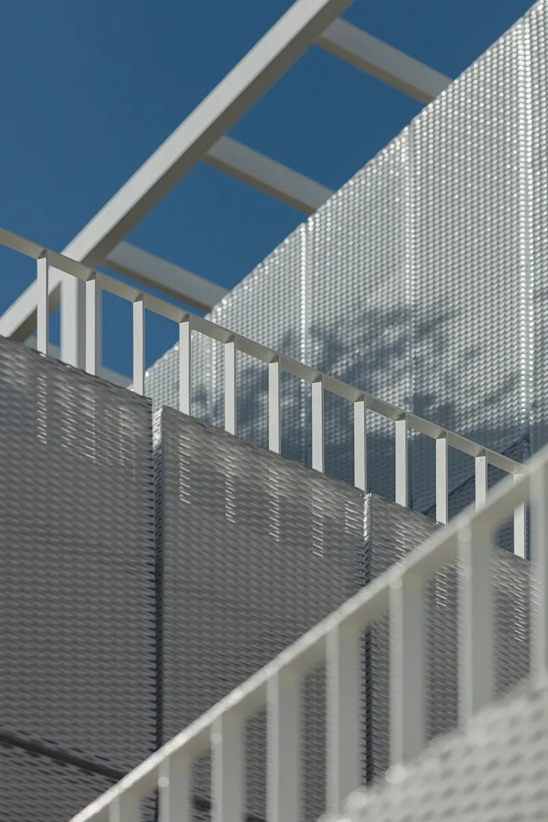 Detail of the white metal pergola frame and layered perforated screen panels under blue sky