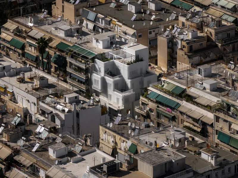 Aerial view of the stepped white volume surrounded by dense rooftops with green awnings