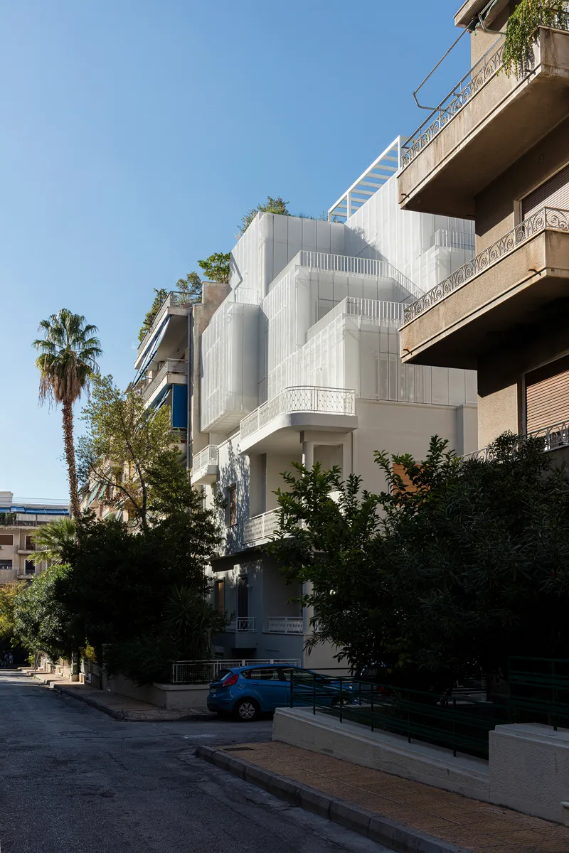 Corner facade showing the textured white stepped volumes beside a palm tree and parked car