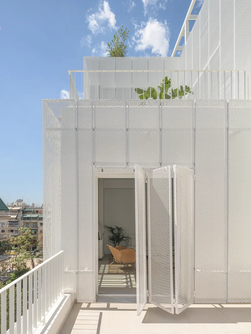 Rooftop terrace with white perforated metal screens, planted bed, and sliding glass door beneath clouds