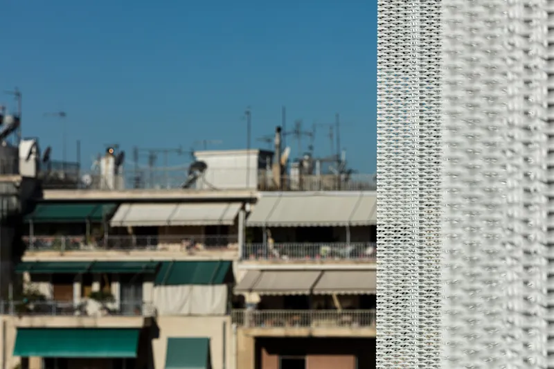 Detail of the textured white screen facade against older residential balconies in the background