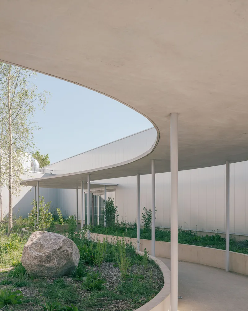 Concrete canopy soffit above the colonnade path with large boulders in the landscape bed