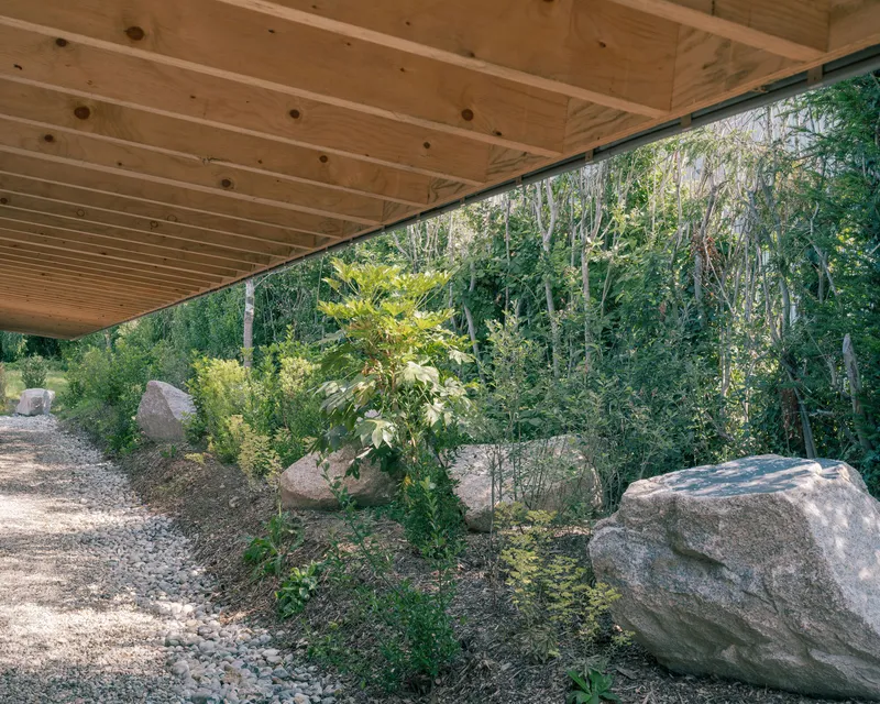 Cantilevered timber roof overhang sheltering a naturalized garden with large stones and native plantings