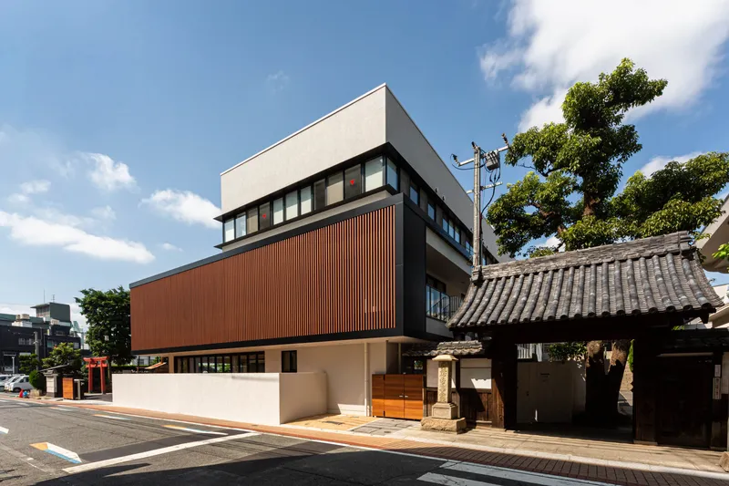 Angled street view showing the timber-clad volume beside a traditional tiled roof structure